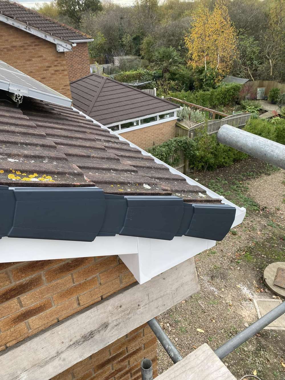 Anthracite dry verge over a white box end at a roof corner, gardens behind