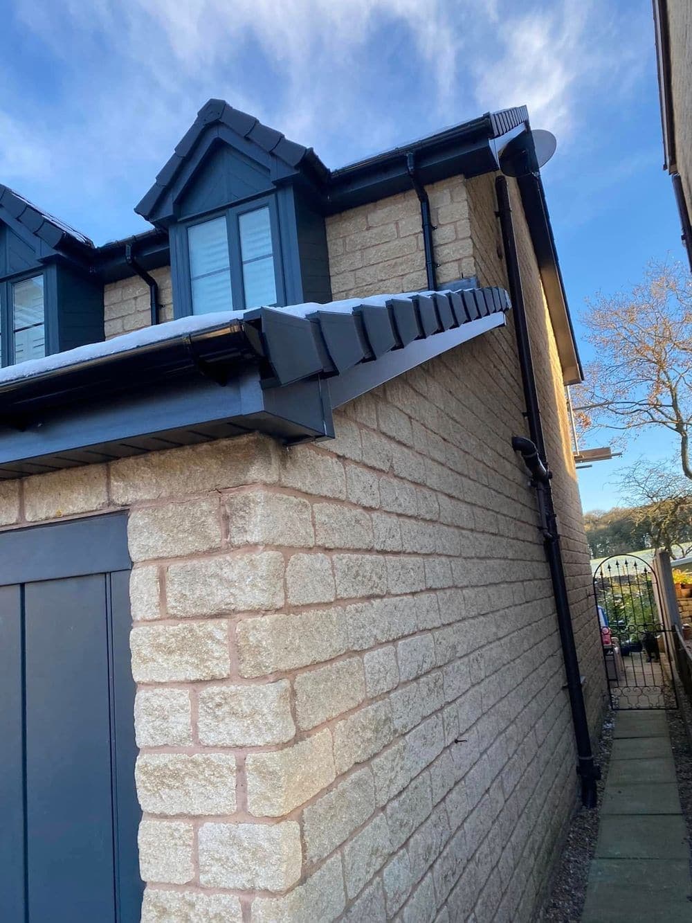 Stone house with dormers and a new anthracite roofline against a blue sky