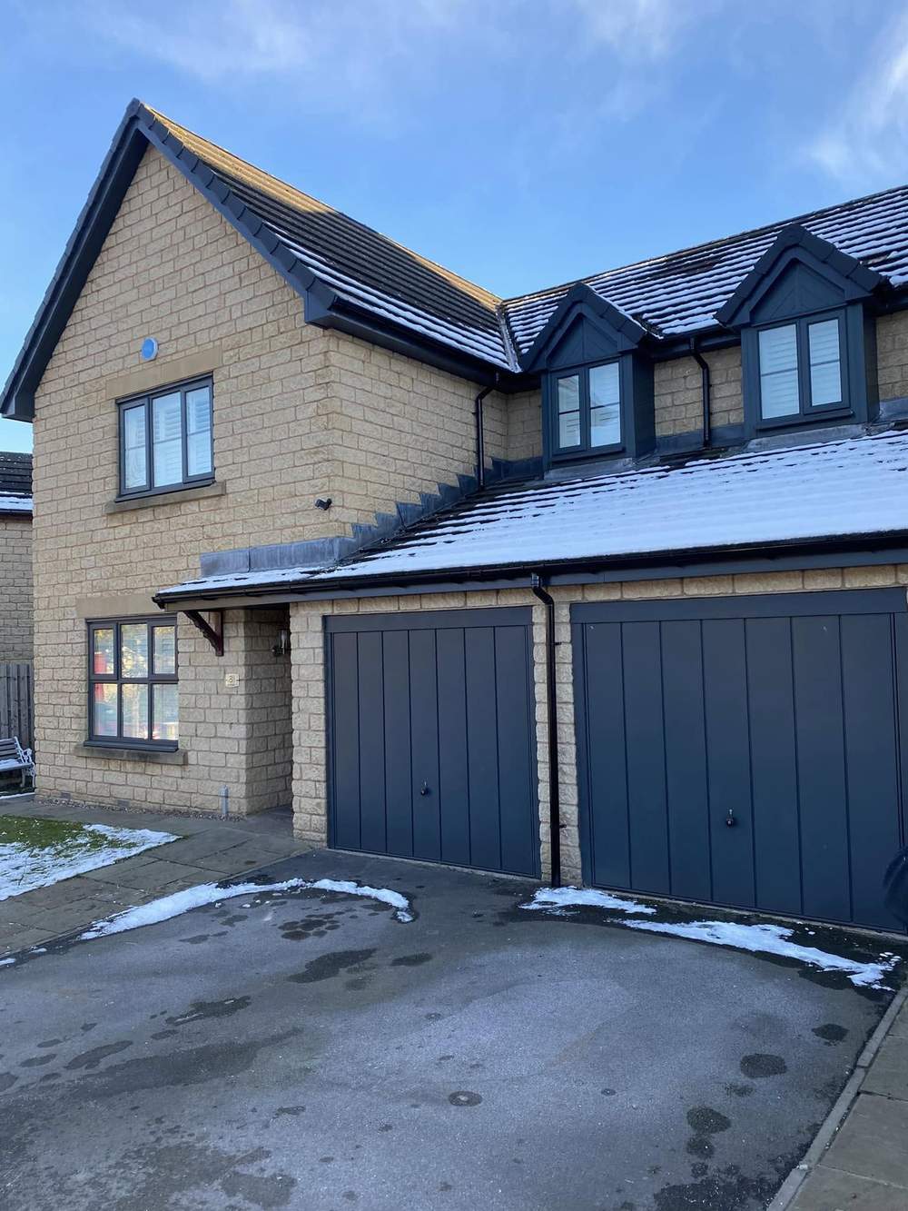 Stone-built detached house with a new anthracite grey fascia, soffit and bargeboards, blue sky behind