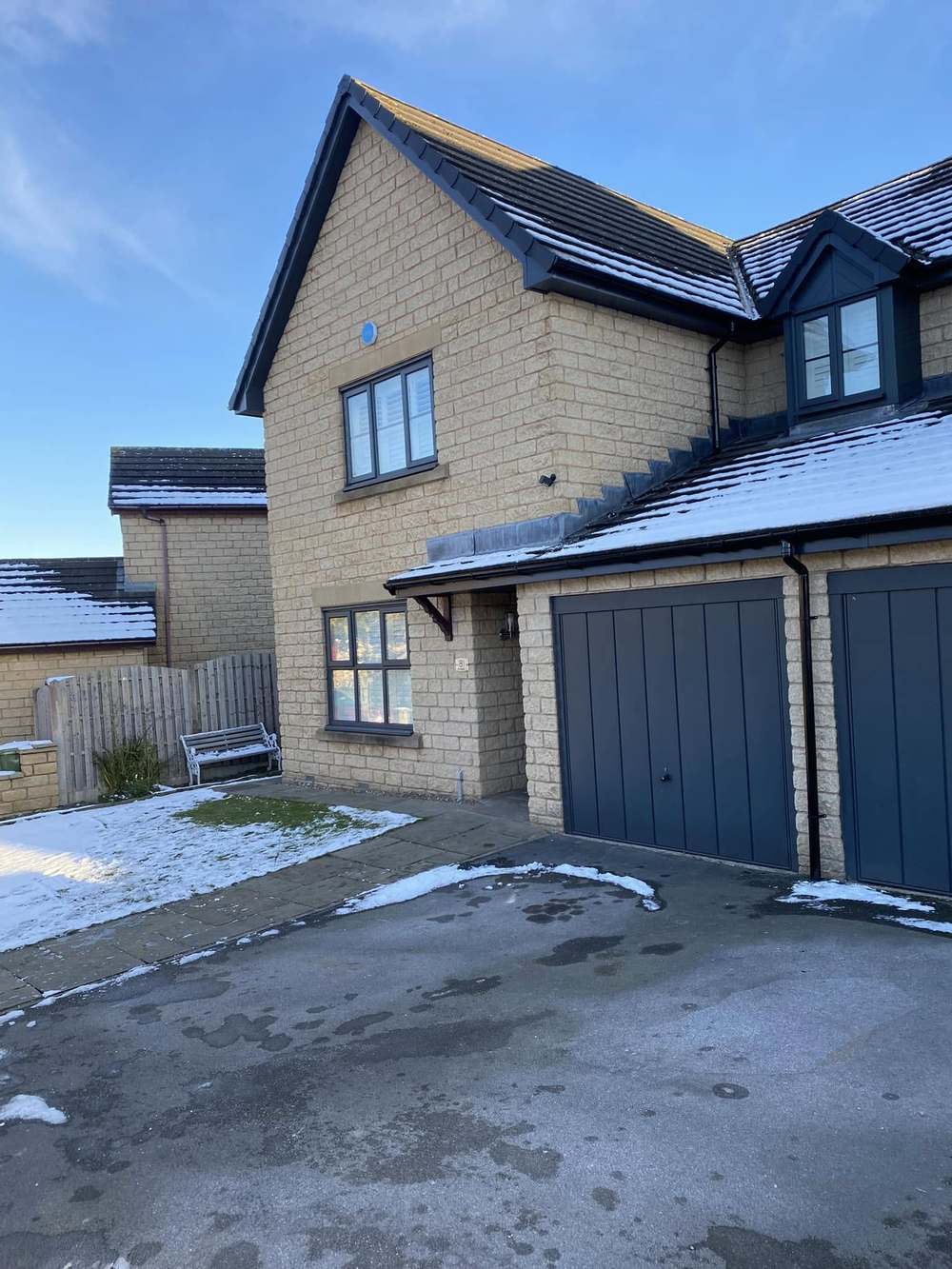 Stone house front with a new anthracite roofline, snow on the drive