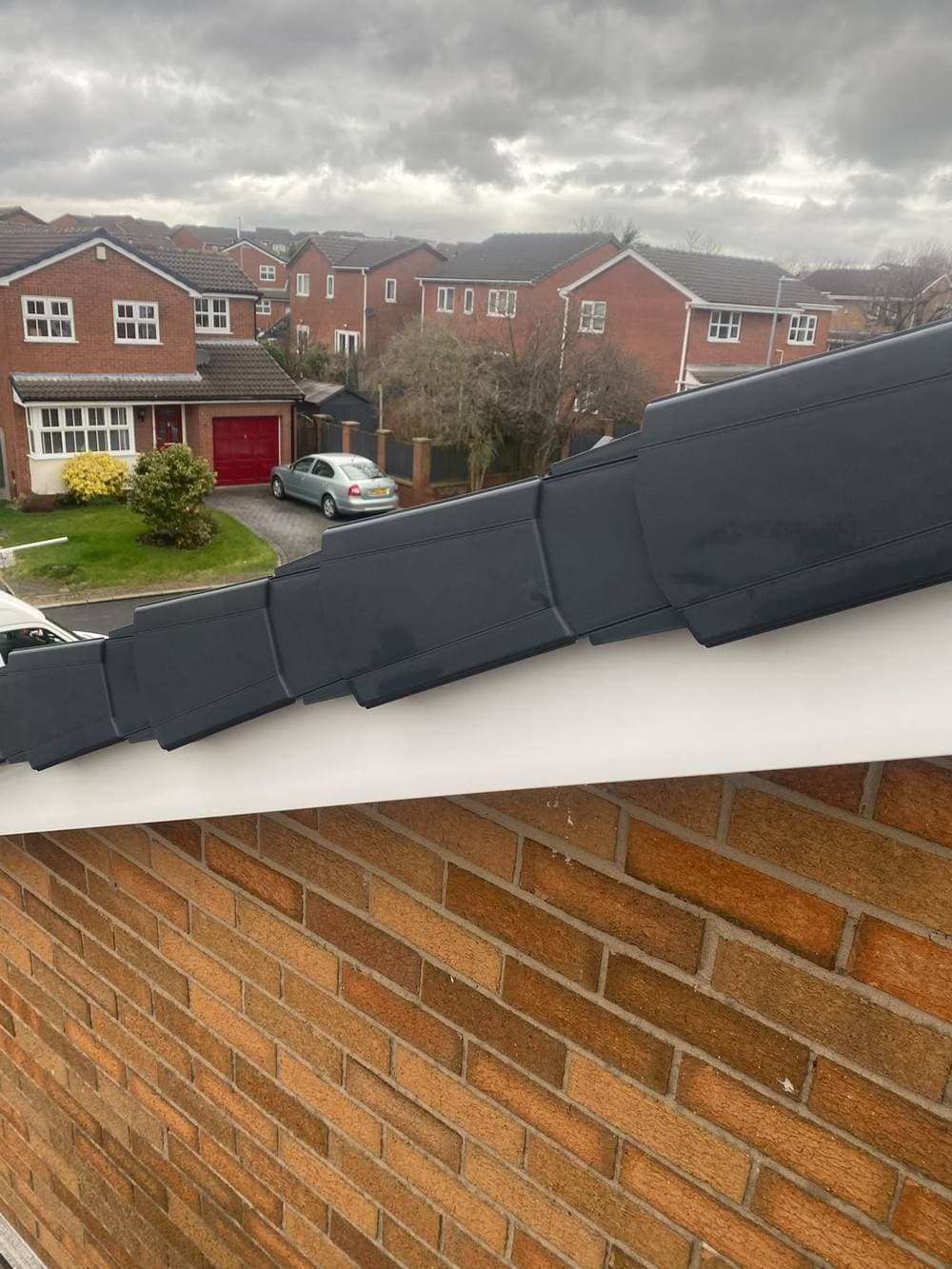 Anthracite dry verge along a gable, houses across the road behind