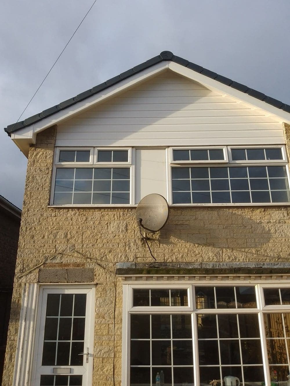 Detached stone-faced house with new white uPVC cladding on the gable and a new roofline