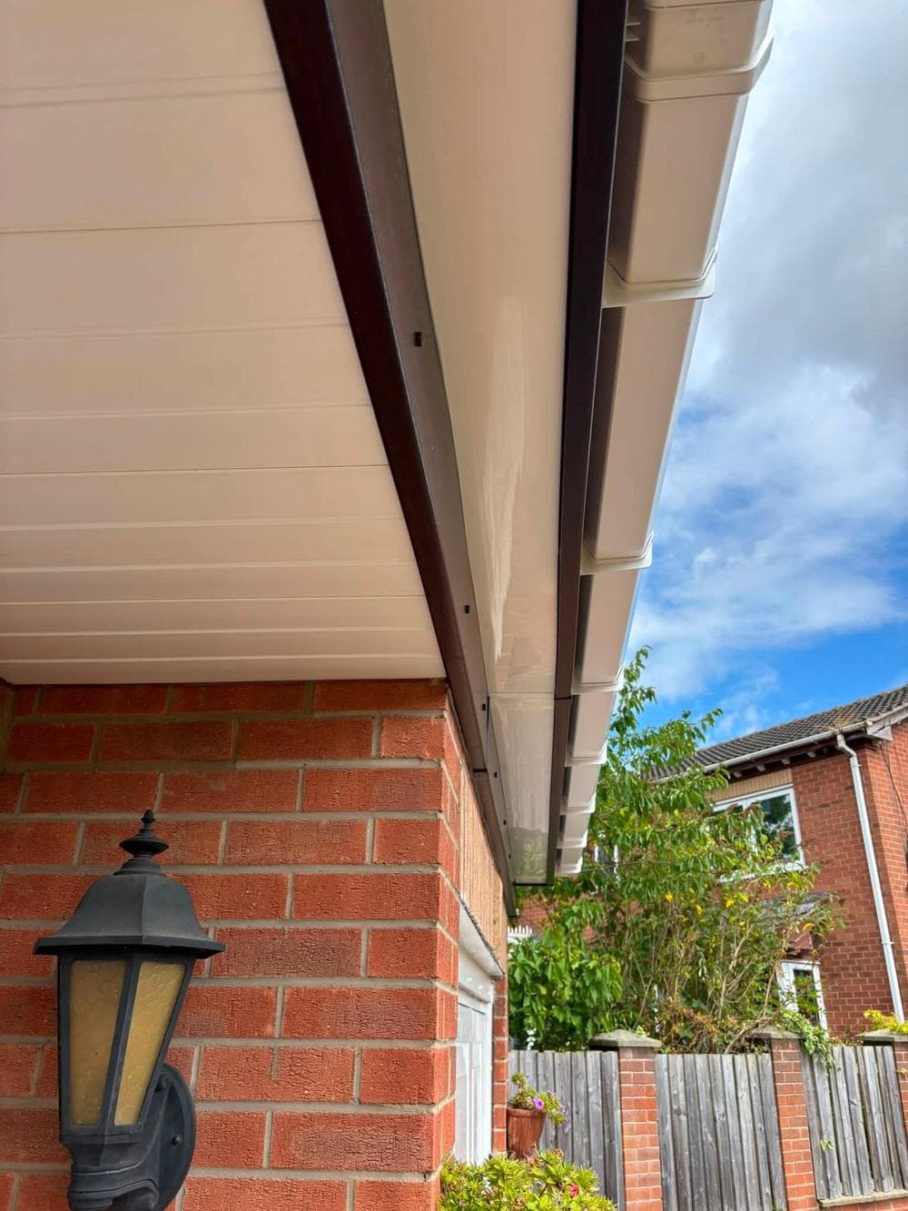 New white soffit under the eaves of a red brick house with a lantern on the wall