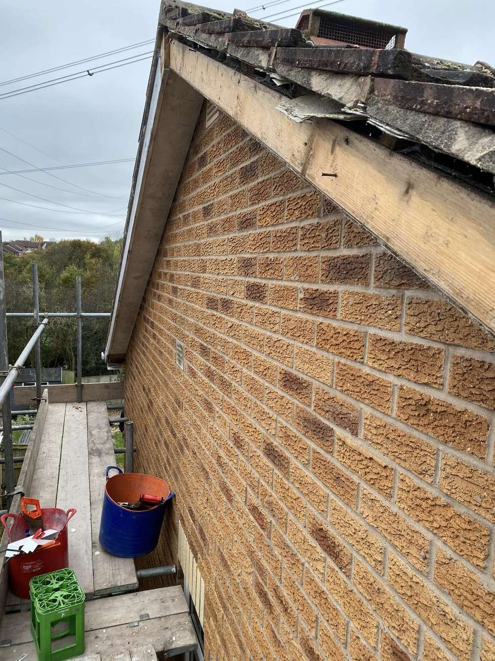 Old timber bargeboard and the rough edge of the tiles on a brick gable, seen from the scaffold before work started