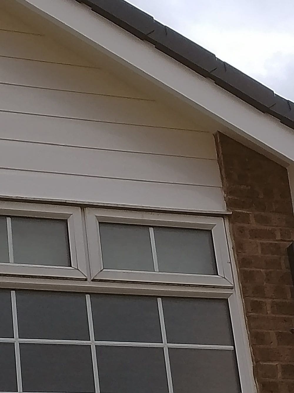 New white uPVC cladding meeting the brick above a window, with a white bargeboard above